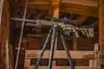 A rifle on top of a tripod in a room.