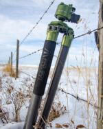 A tripod leaning up against a barbed wire fence.