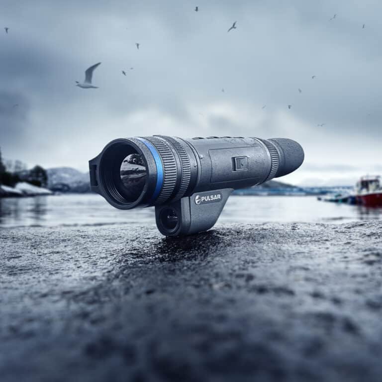 A telescope sitting on the ground in front of water.