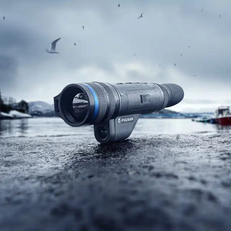 A telescope sitting on the ground in front of water.