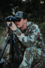 A man in camouflage jacket looking through binoculars.