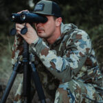 A man in camouflage jacket looking through binoculars.