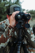 A man in camouflage is looking through binoculars.