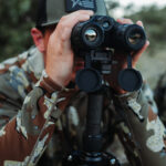 A man in camouflage is looking through binoculars.